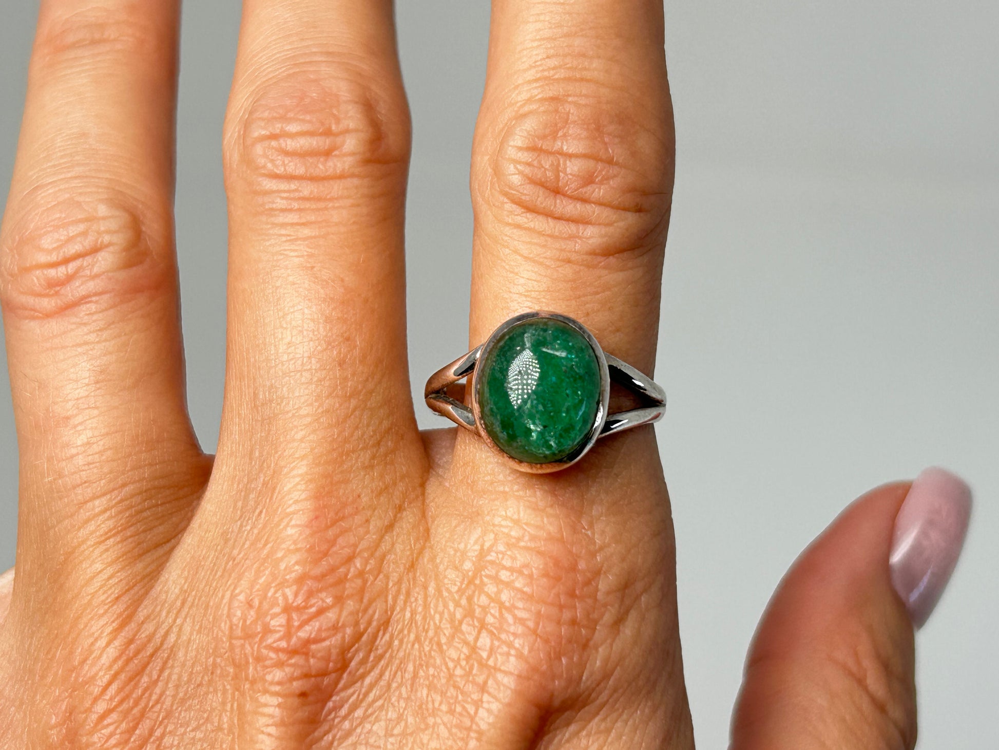 Hand wearing an Emerald Tanzurine Sterling Silver Ring for spiritual healing against white background.