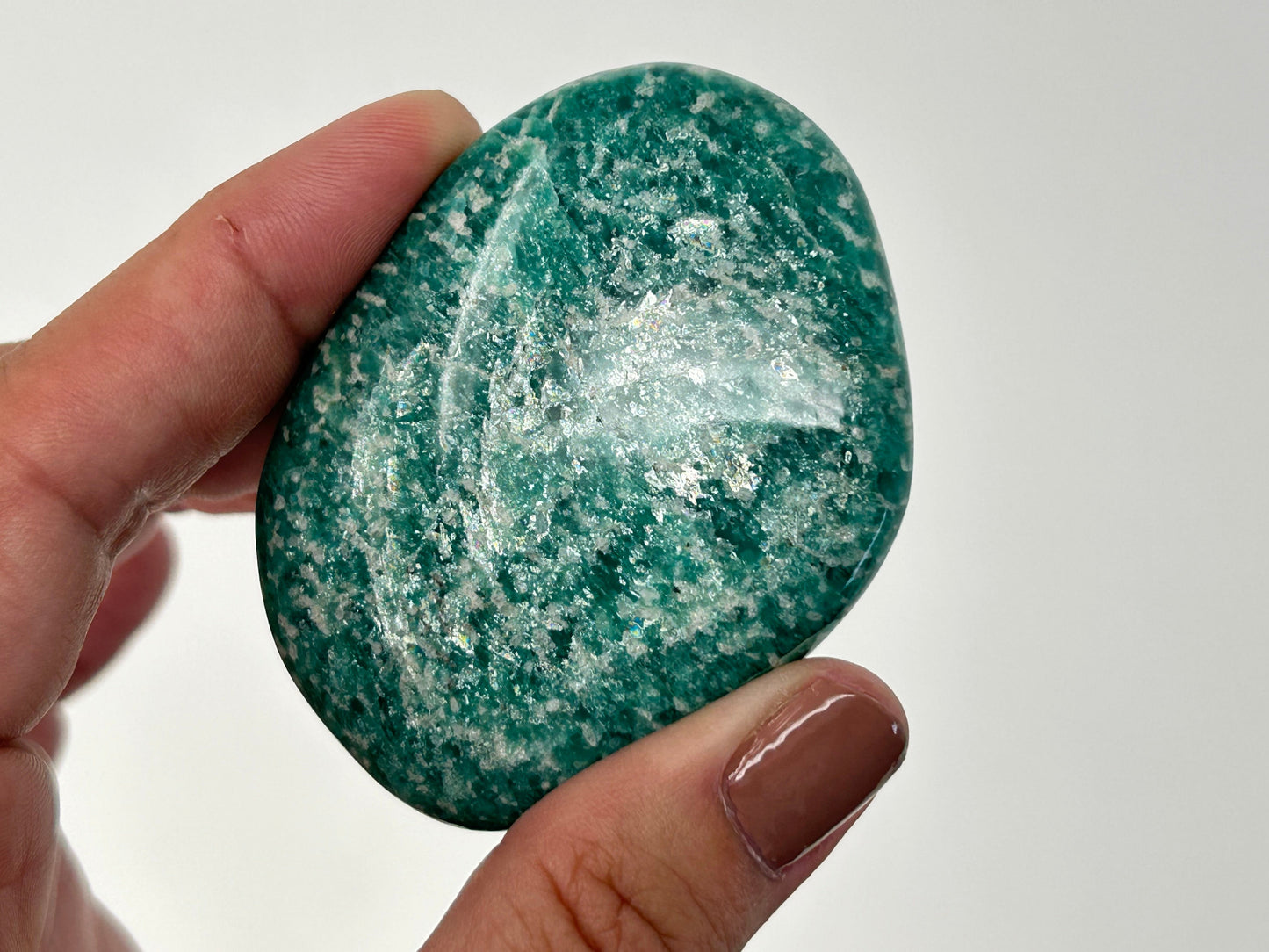 Hand holding a white speckled Energized Emerald Green Amazonite Palm Stone against a plain background