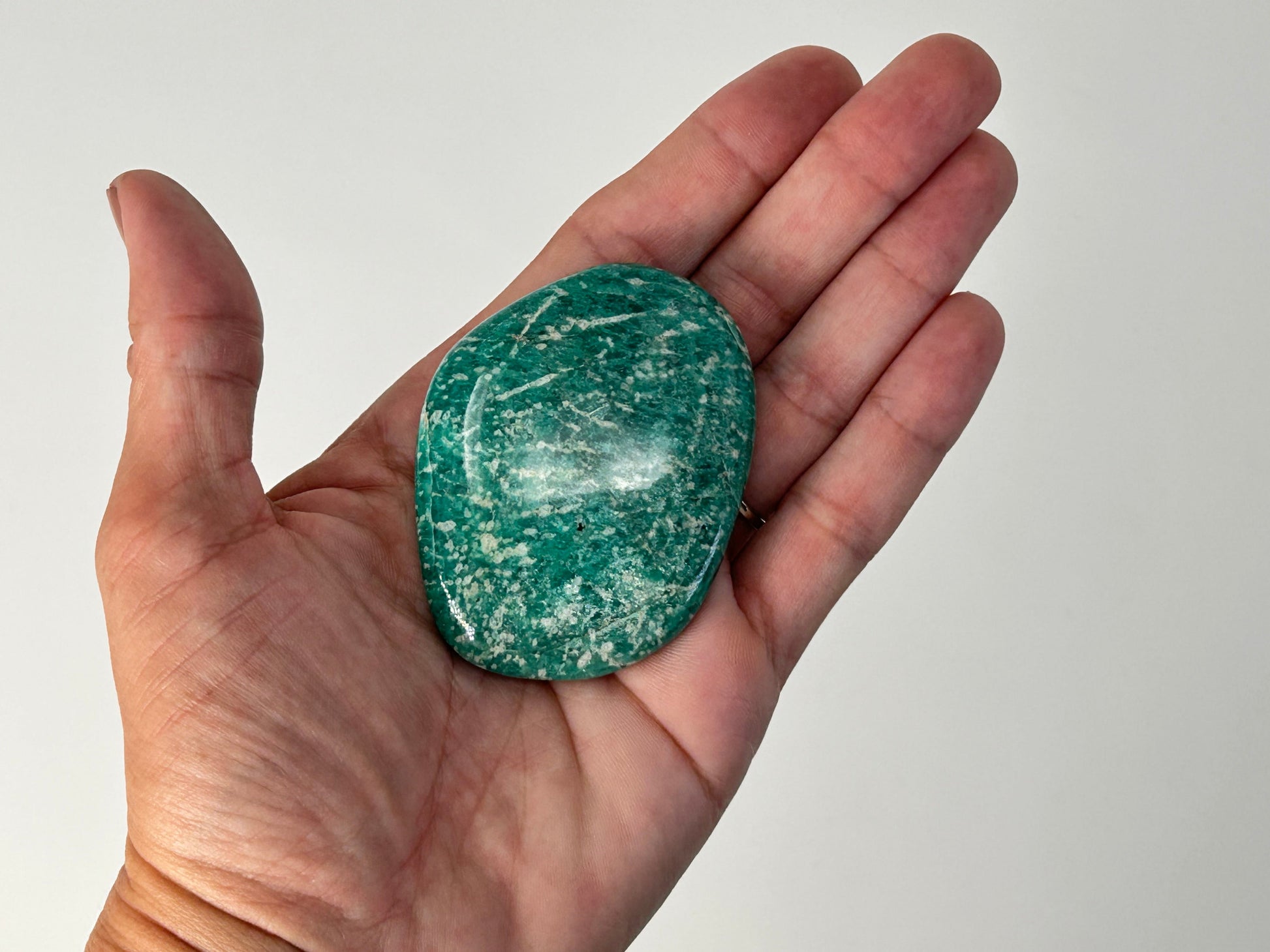 Hand holding a Energized Emerald Green Amazonite Palm Stone against a plain background