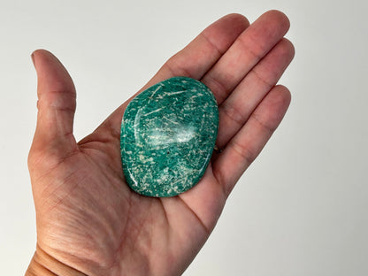 Hand holding a Energized Emerald Green Amazonite Palm Stone against a plain background