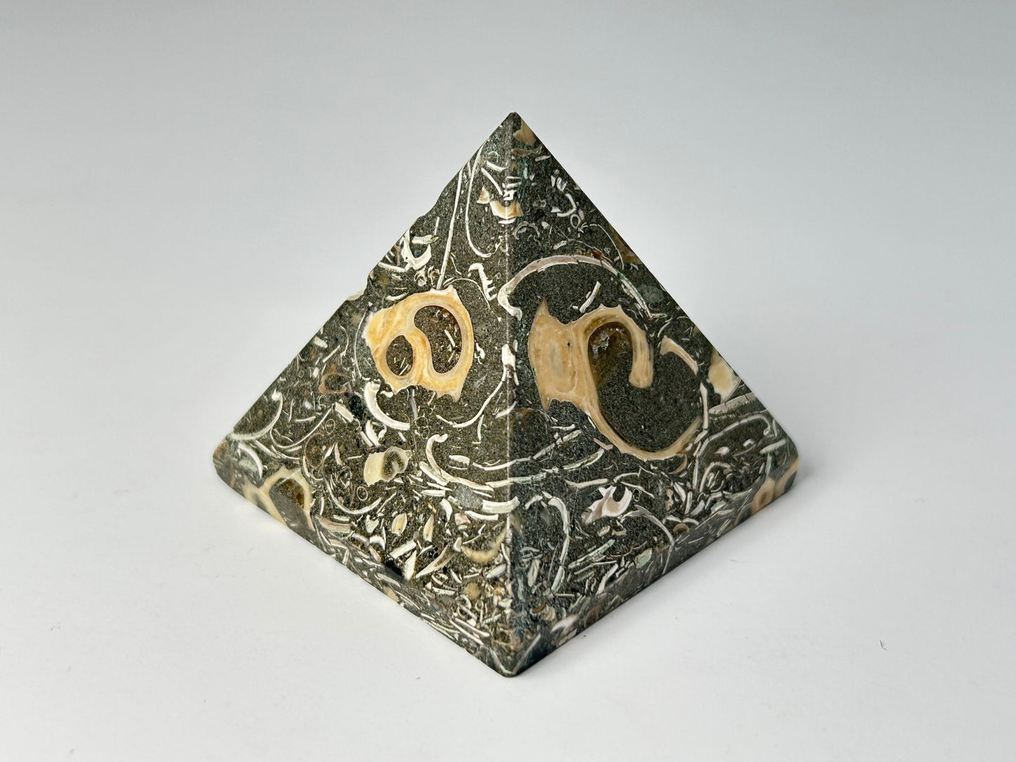 Grounding Turritella Agate Pyramid with engraved symbols on a gray background