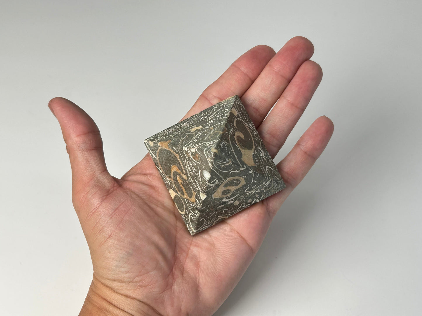 Hand holding a marbled stone Grounding Turritella Agate Pyramid against a plain background