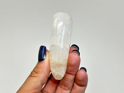 A hand holding a polished white High-Vibrational Natrolite Freeform against a plain light gray background.