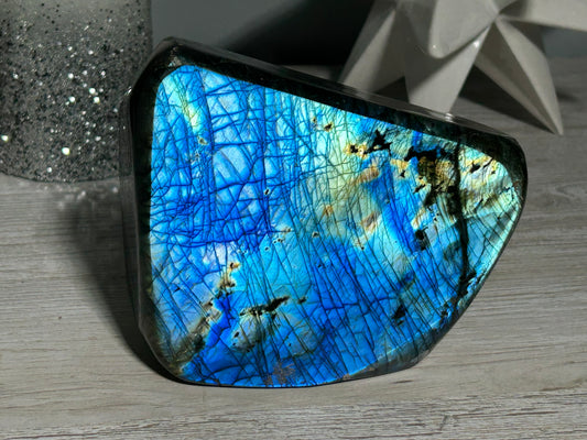 Labradorite freeform-shaped crystal with blue flash intuition protection displaying blue and silver colors, placed on a wooden surface.