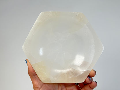 Hand holding a Light-filled Octagon Selenite Bowl for meditation and energy work with white background
