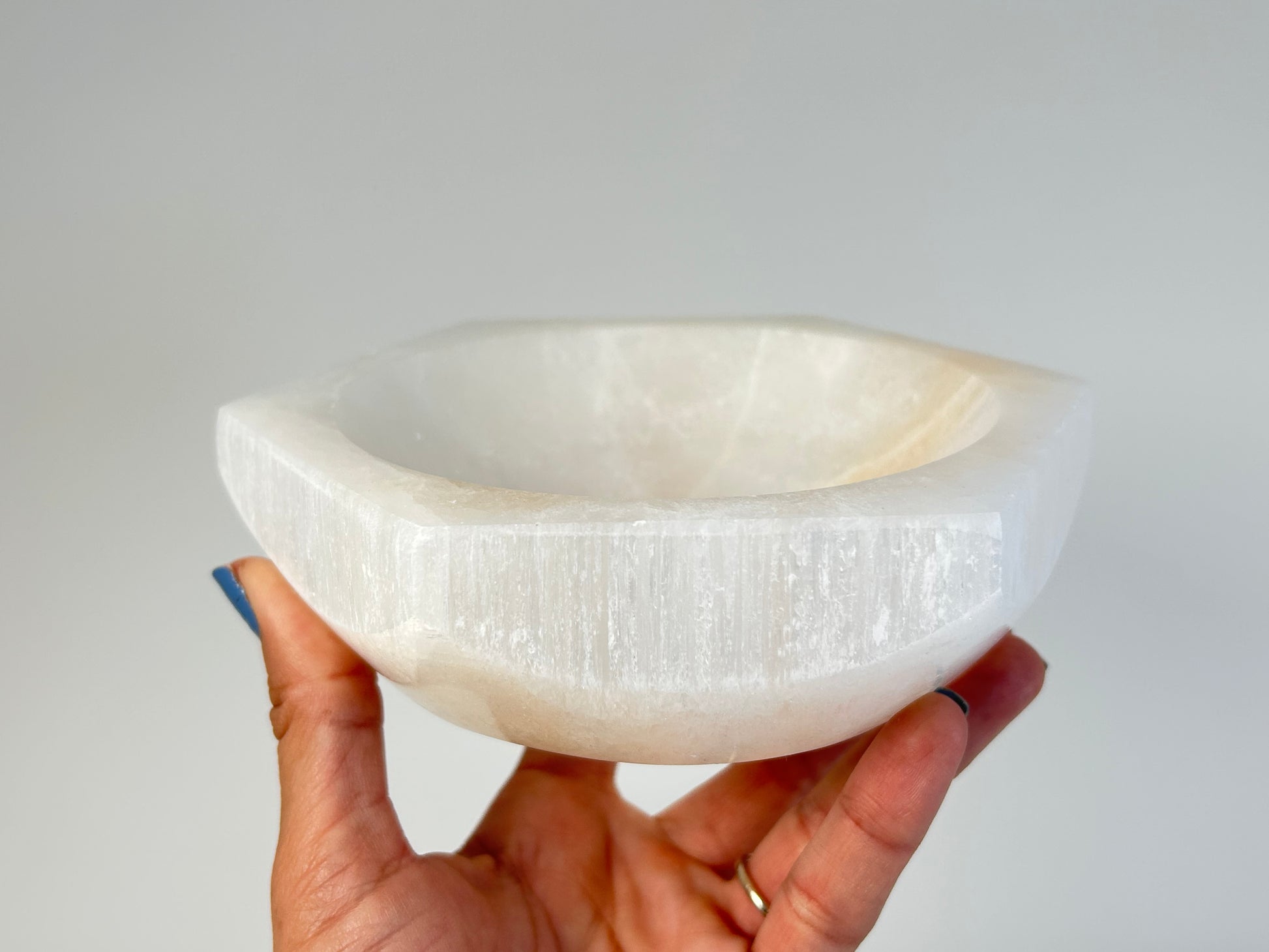 Hand holding a Light-filled Octagon Selenite Bowl with white background.
