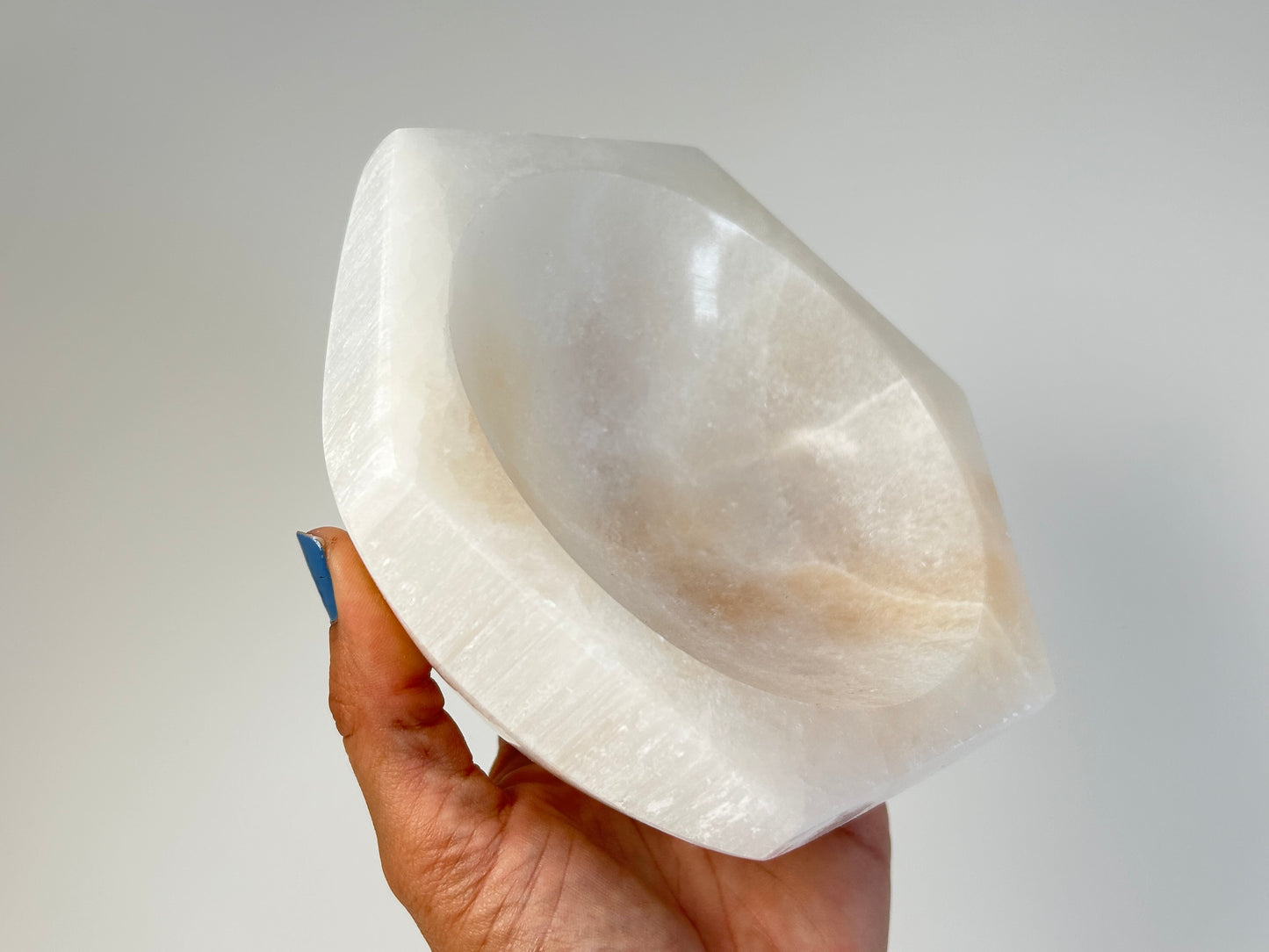 Hand holding a Light-filled Octagon Selenite Bowl on table top with white background
