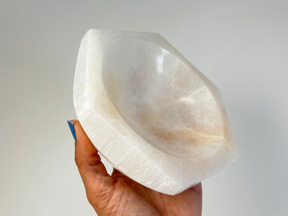 Hand holding a Light-filled Octagon Selenite Bowl on table top with white background
