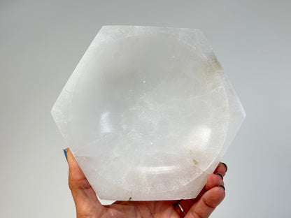Hand holding a ethically sourced light-filled Octagon Selenite Bowl for meditation over white background
