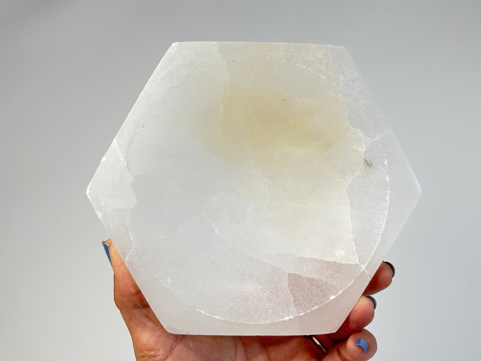 Hand holding a Light-filled Octagon Selenite Bowl for spiritual healing against white background
