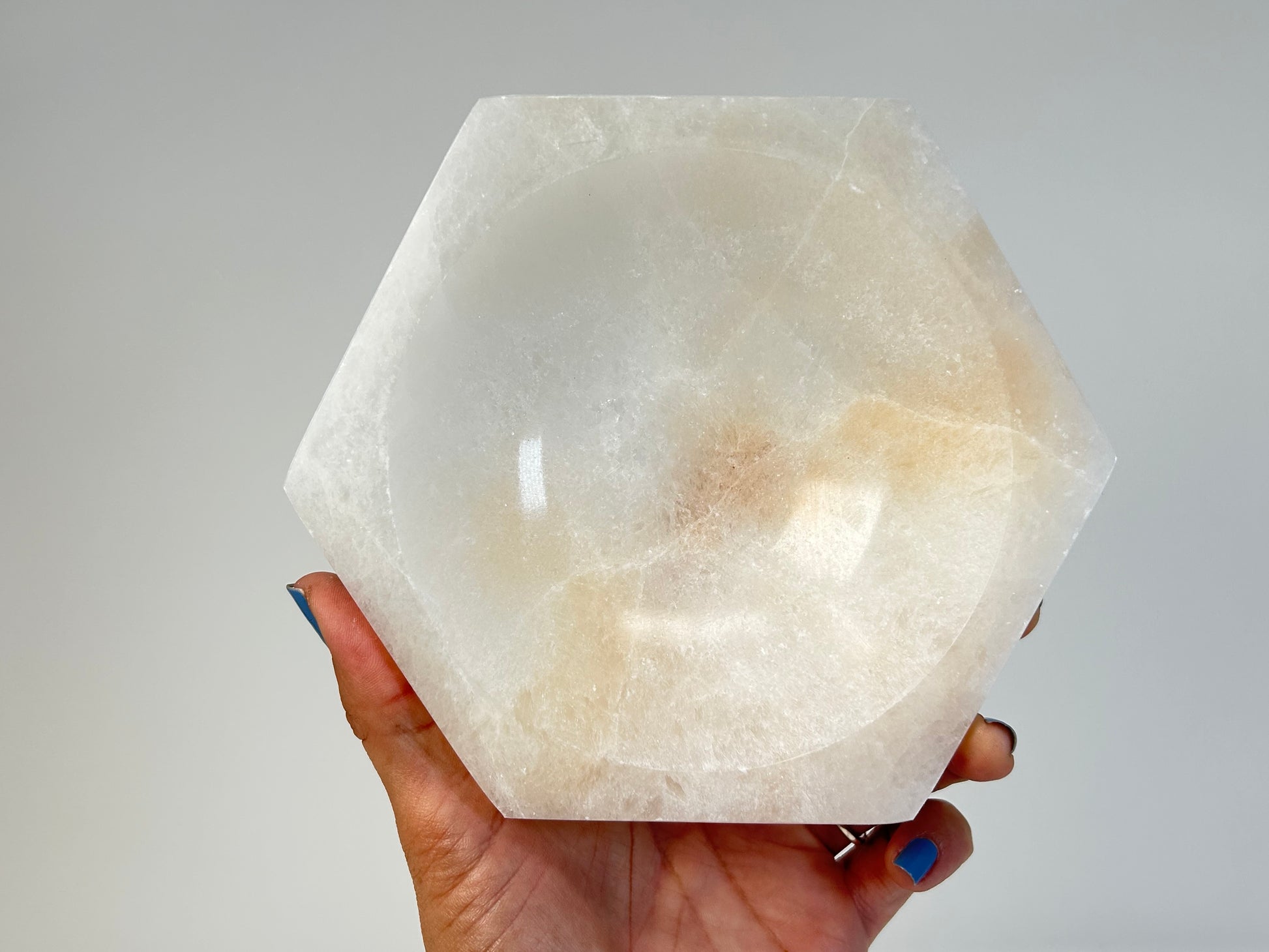 Hand holding a Light-filled Octagon Selenite Bowl for natural grounding crystal healing stone with white background