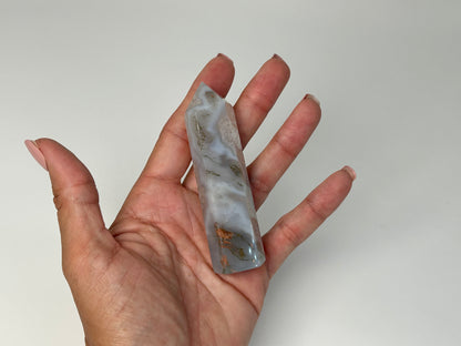 Hand holding a Moss Agate Crystal Tower with a white background