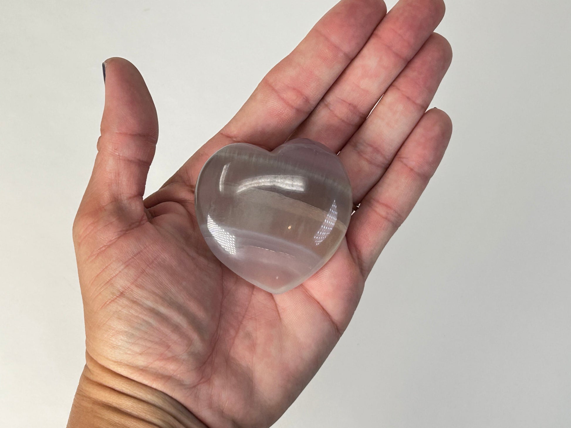 A translucent heart-shaped Naturally Striped Fluorite Heart held in a person's open palm against a plain light background.