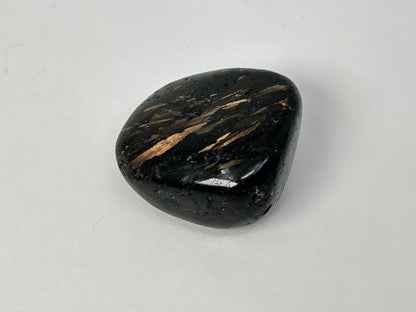 A polished black Nuummite Tumbled crystal with distinctive metallic copper-gold streaks, photographed on a neutral light gray background.
