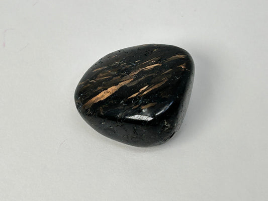 A polished black Nuummite Tumbled crystal with distinctive metallic copper-gold streaks, photographed on a neutral light gray background.