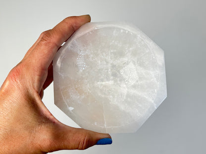 Hand holding a Octagon Selenite Bowl from Morocco for spiritual healing against white background