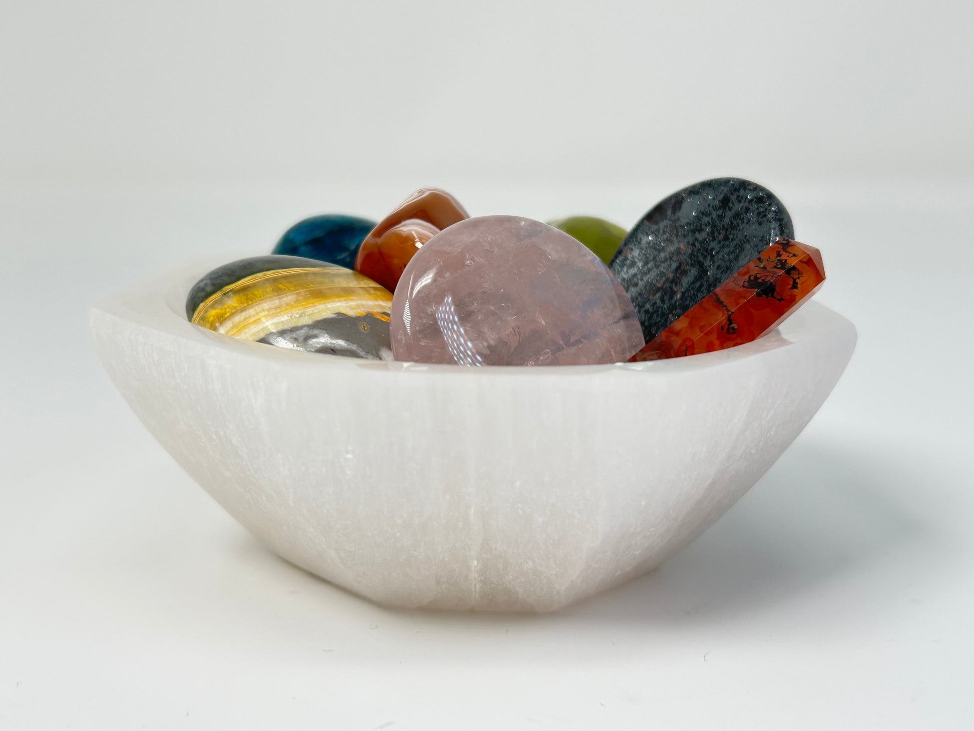 White Octagon Selenite Bowl from Morocco for meditation and energy work filled with multicolored crystals on a white background