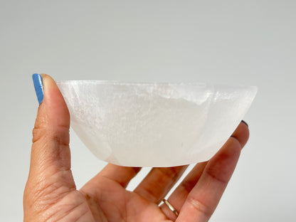 Hand holding a ethically sourced Octagon Selenite Bowl from Morocco for meditation over white background