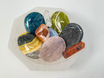 Collection of multicolored stones in a Octagon Selenite Bowl from Morocco for energy healing on a white background