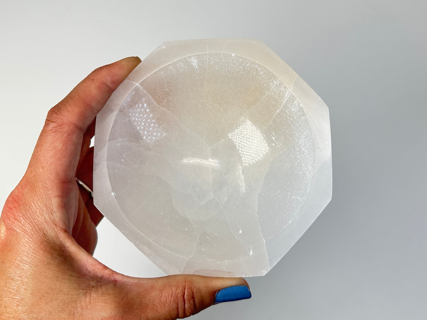 Hand holding a Octagon Selenite Bowl from Morocco with white background.