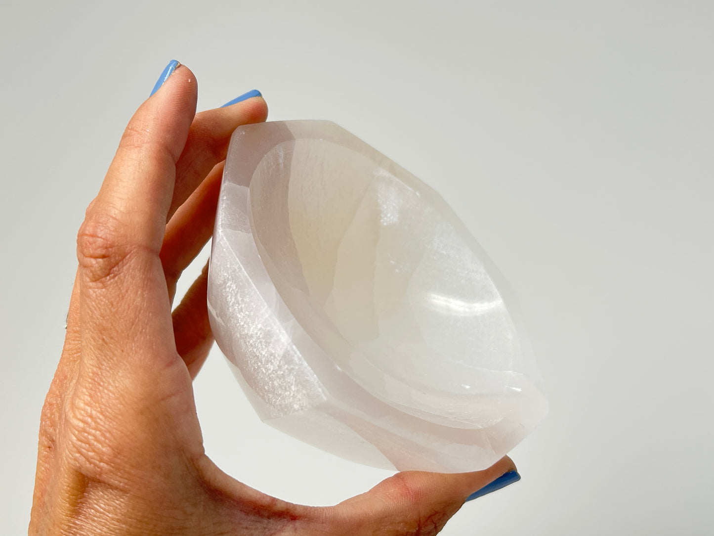 Hand holding a Octagon Selenite Bowl from Morocco on table top with white background