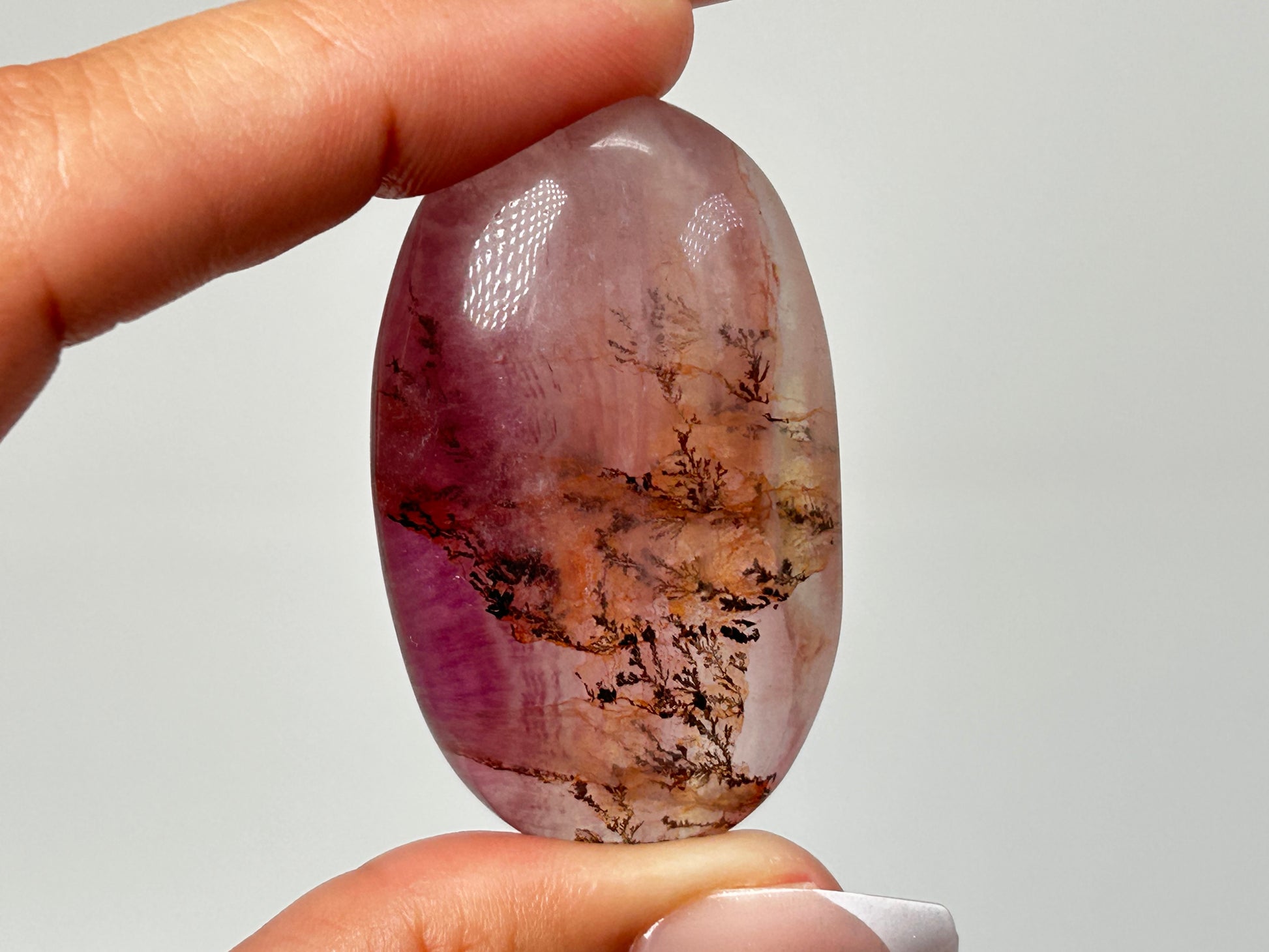 Hand holding a Oval-shaped Brown Organic Dendritic Fluorite Palm Stone chakra balancing gemstone for spiritual healing crystal against white background.
