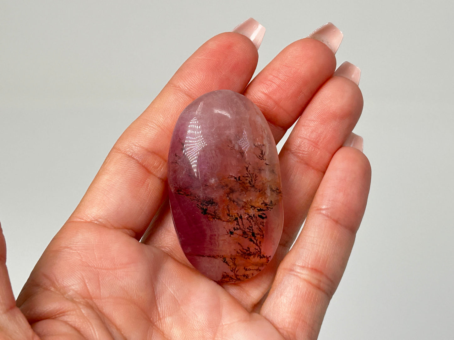 Hand holding Oval-shaped Brown Organic Dendritic Fluorite Palm Stone reiki charged healing crystal with white background.