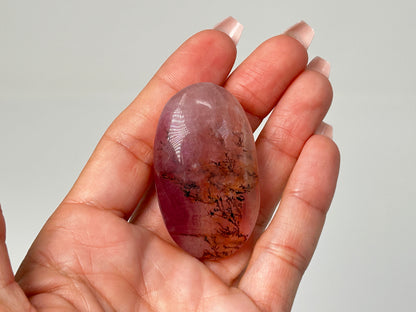 Hand holding Oval-shaped Brown Organic Dendritic Fluorite Palm Stone reiki charged healing crystal with white background.
