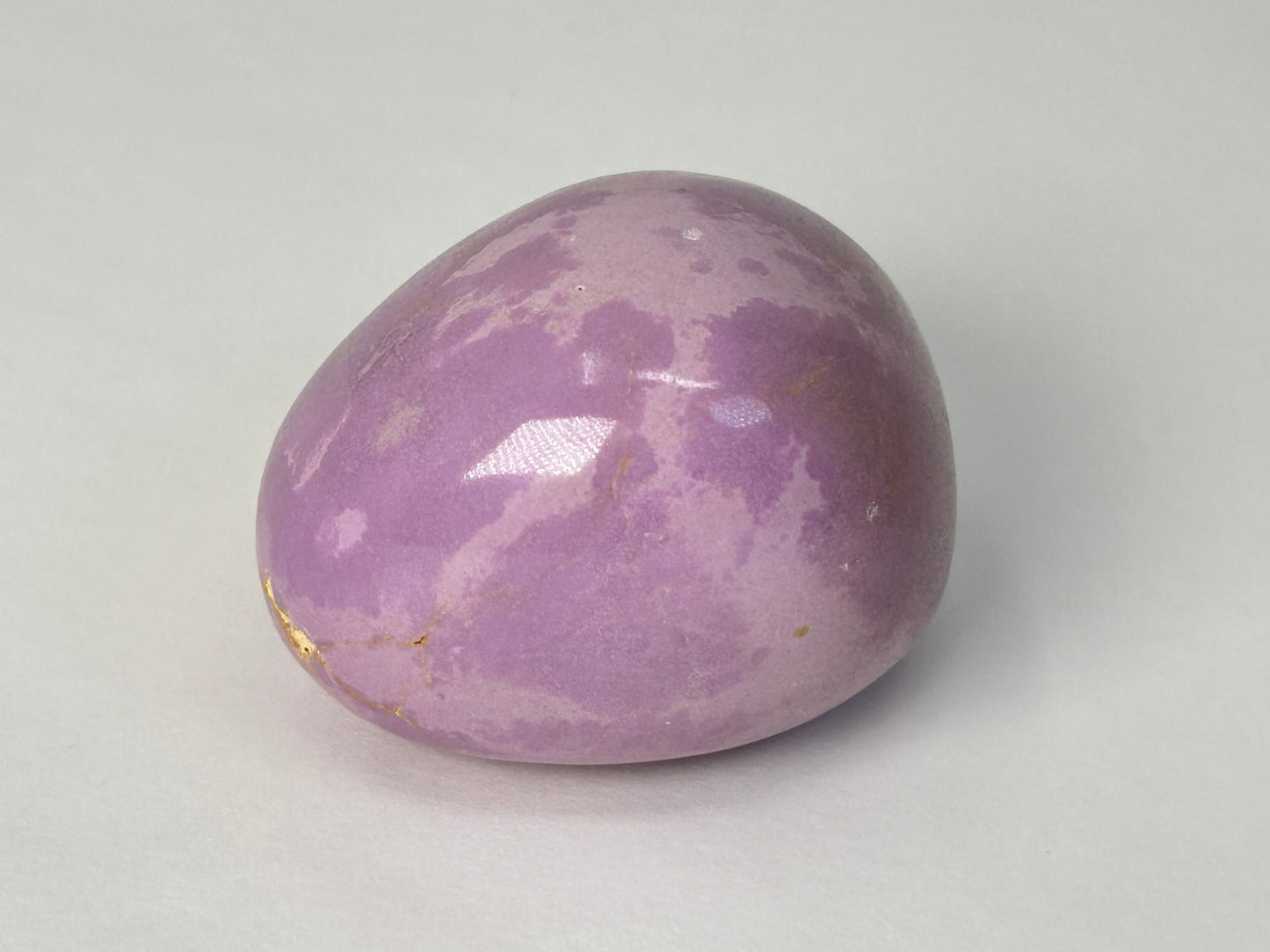 A polished purple Phosphosiderite Compassion Pebble with natural marbled patterns, photographed on a neutral light gray background.