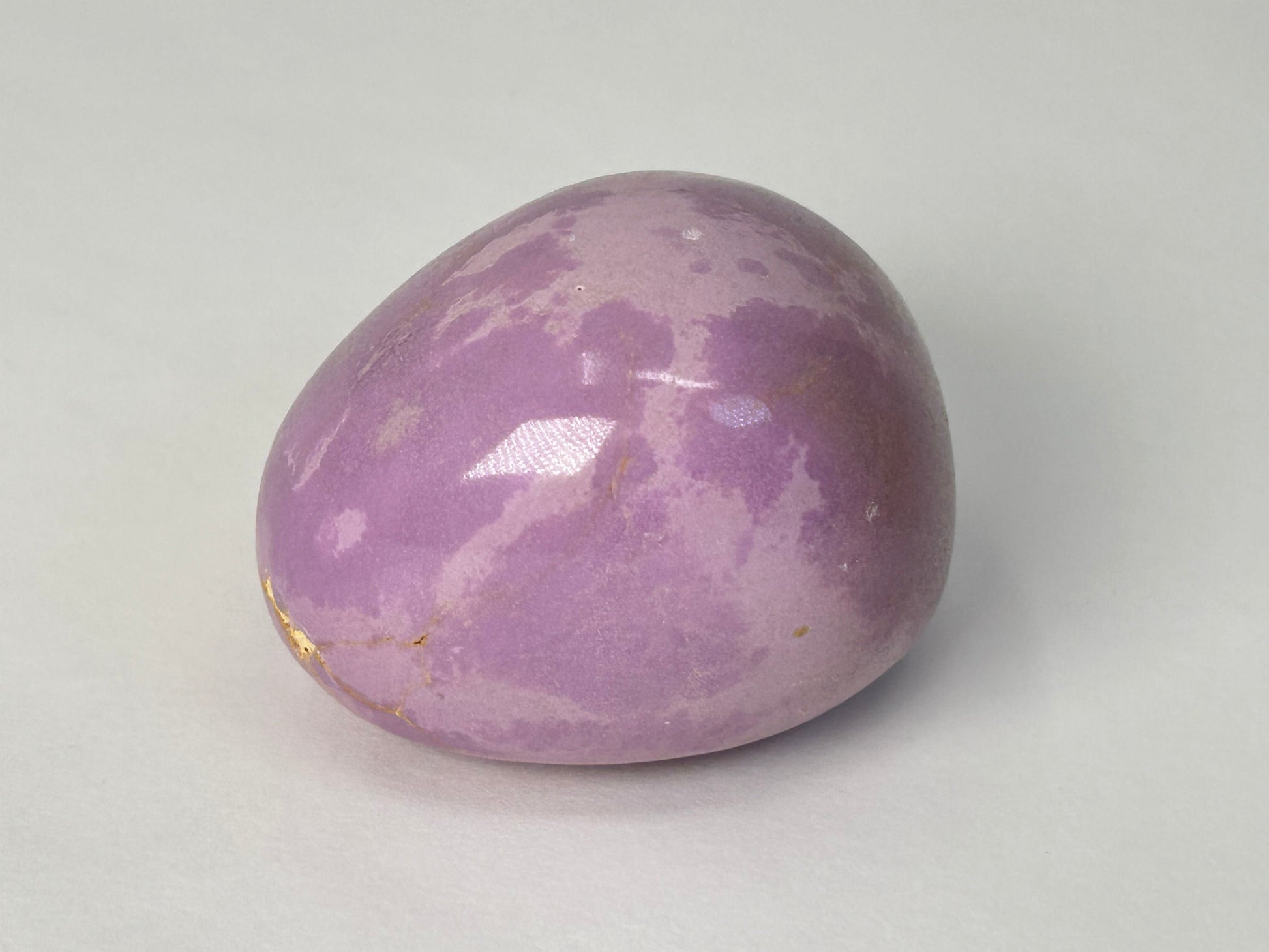 A polished purple Phosphosiderite Compassion Pebble with natural marbled patterns, photographed on a neutral light gray background.