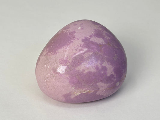 A smooth, polished purple Phosphosiderite Compassion Pebble with natural marbled patterns, photographed on a neutral light gray background.