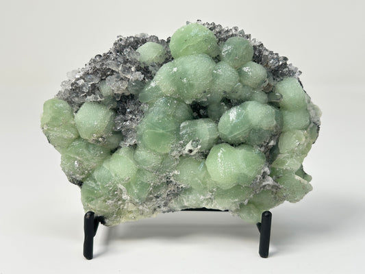 Prehnite on Quartz Cluster in stand on table top with white background