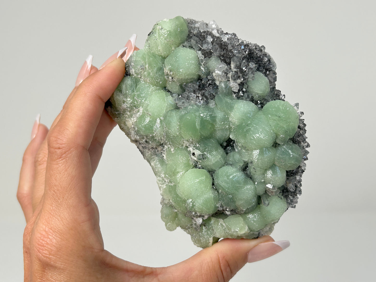 Hand holding a beautiful Prehnite on Quartz Cluster ethically sourced natural healing crystal gemstone for meditation over white background.