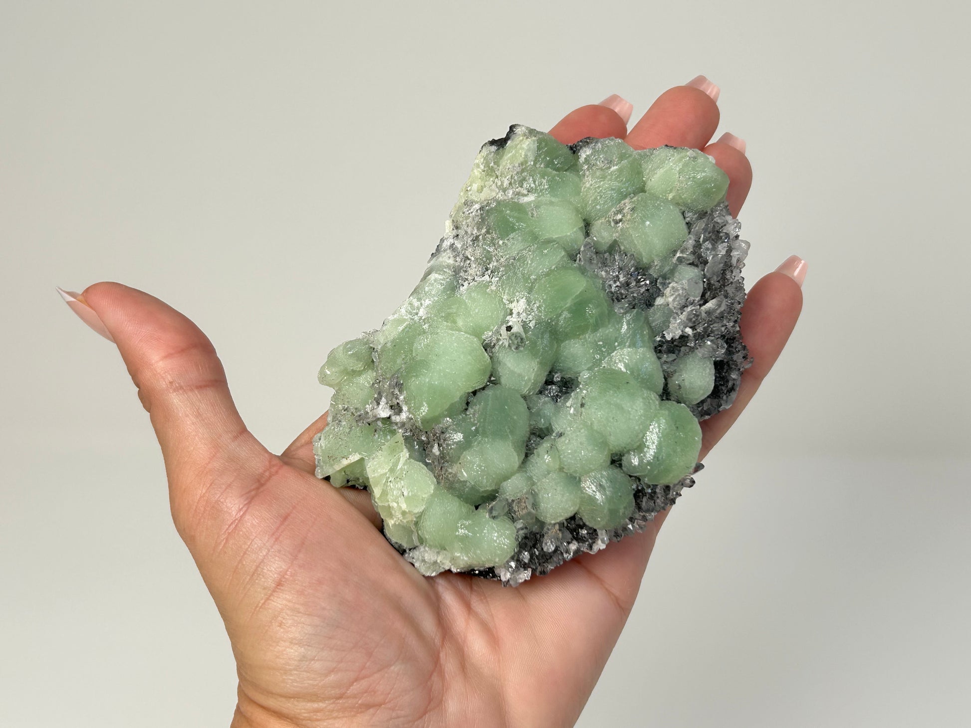 Hand holding a Prehnite on Quartz Cluster chakra balancing gemstone for spiritual healing crystal against white background.