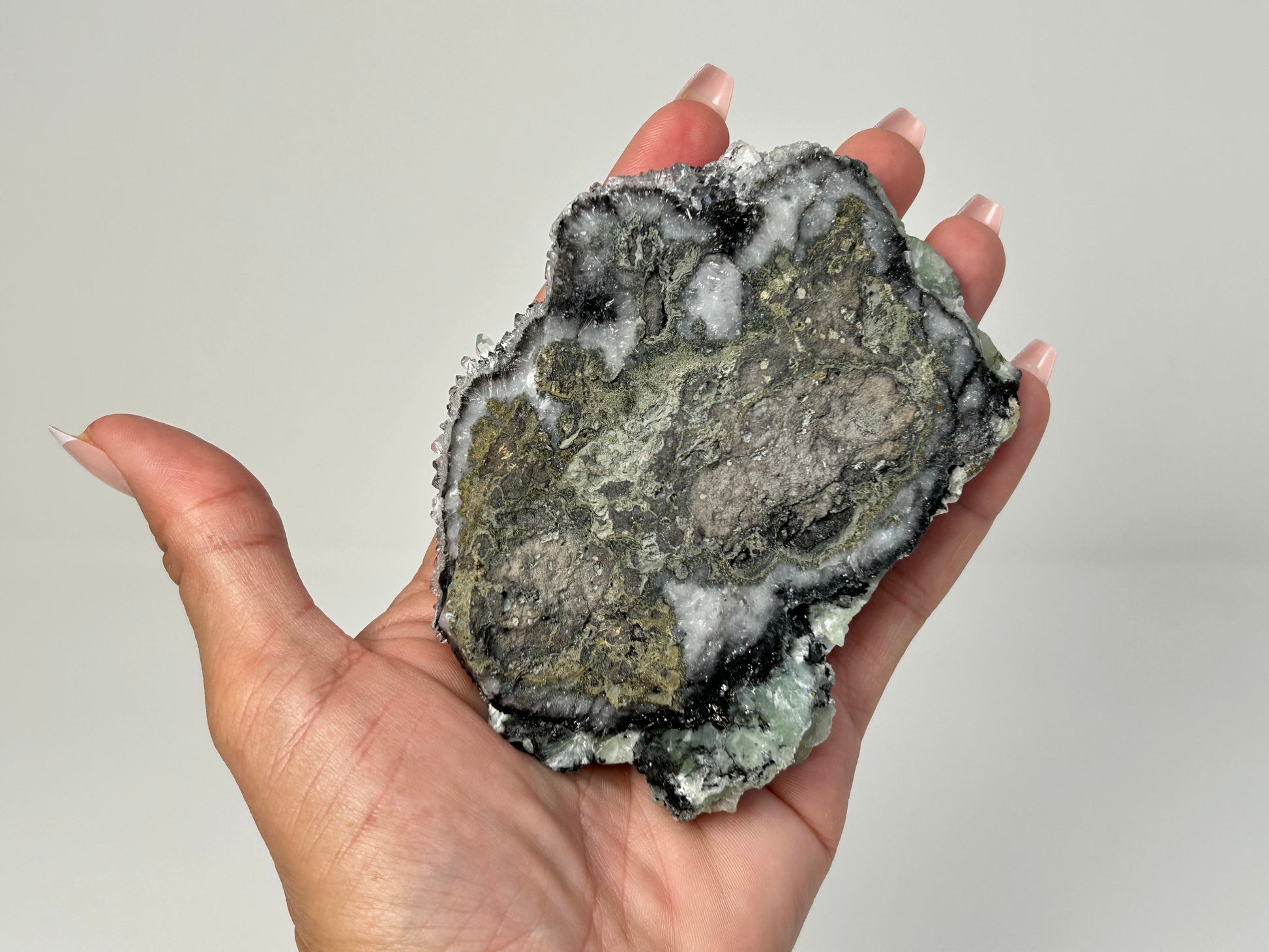 Hand holding a Prehnite on Quartz Cluster healing crystal gemstone for meditation and energy work with white background.