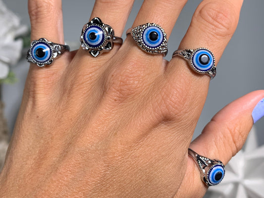 A close-up of a hand wearing five silver rings, each featuring a blue and black evil eye design.