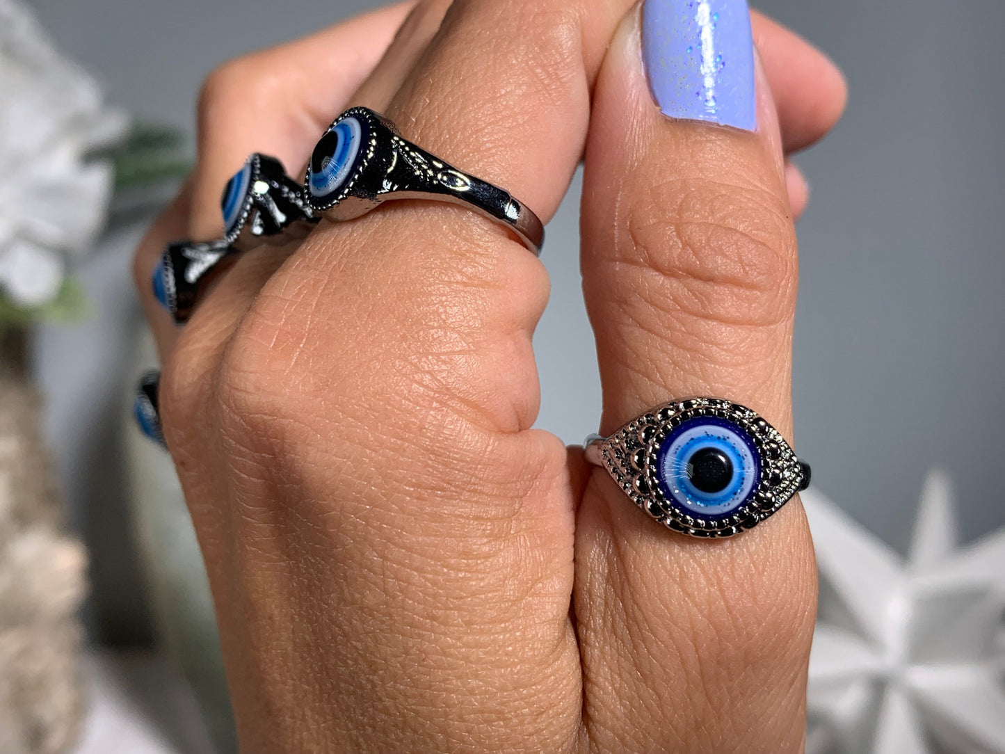 Close-up of hand with Protect Your Peace Silver Evil Eye Rings for energy and trust against a white gray floral background