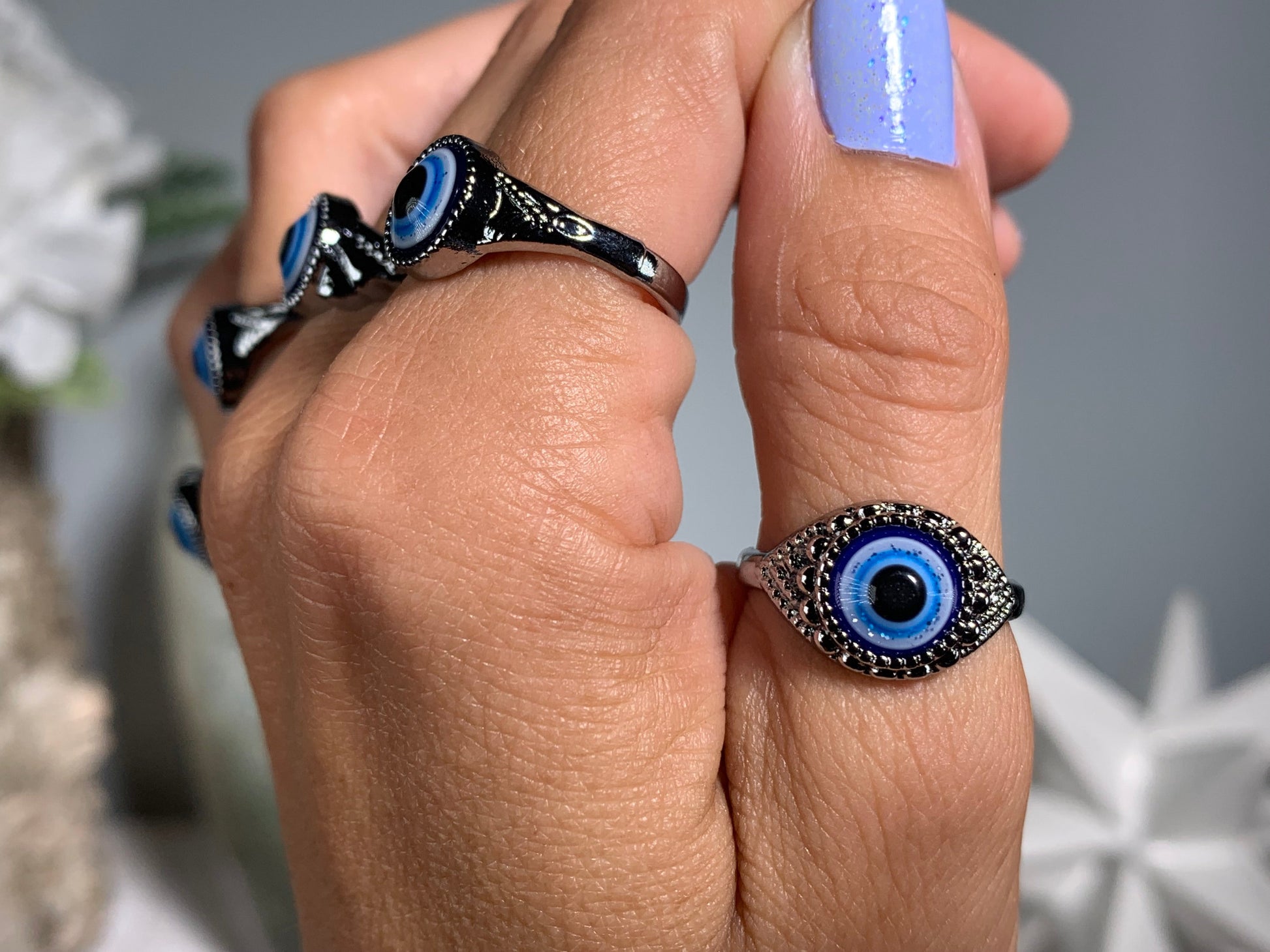 Close-up of hand with Protect Your Peace Silver Evil Eye Rings for energy and trust against a white gray floral background
