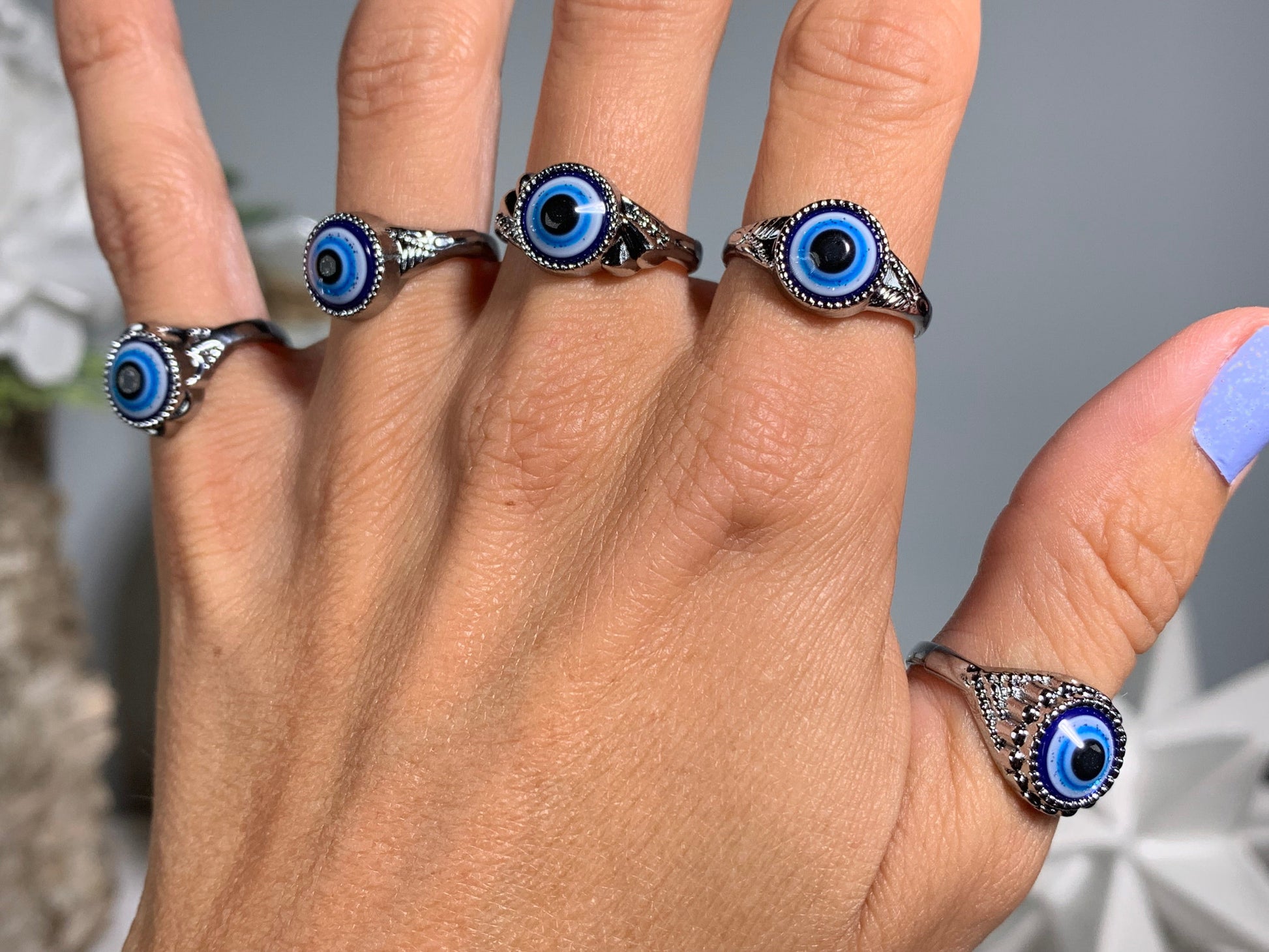 Close-up of hand with Protect Your Peace Silver Evil Eye Rings for energy and trust against a white gray floral background
