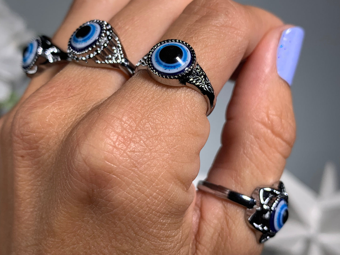 Close-up of hand with Protect Your Peace Silver Evil Eye Rings for energy and trust against a white gray floral background