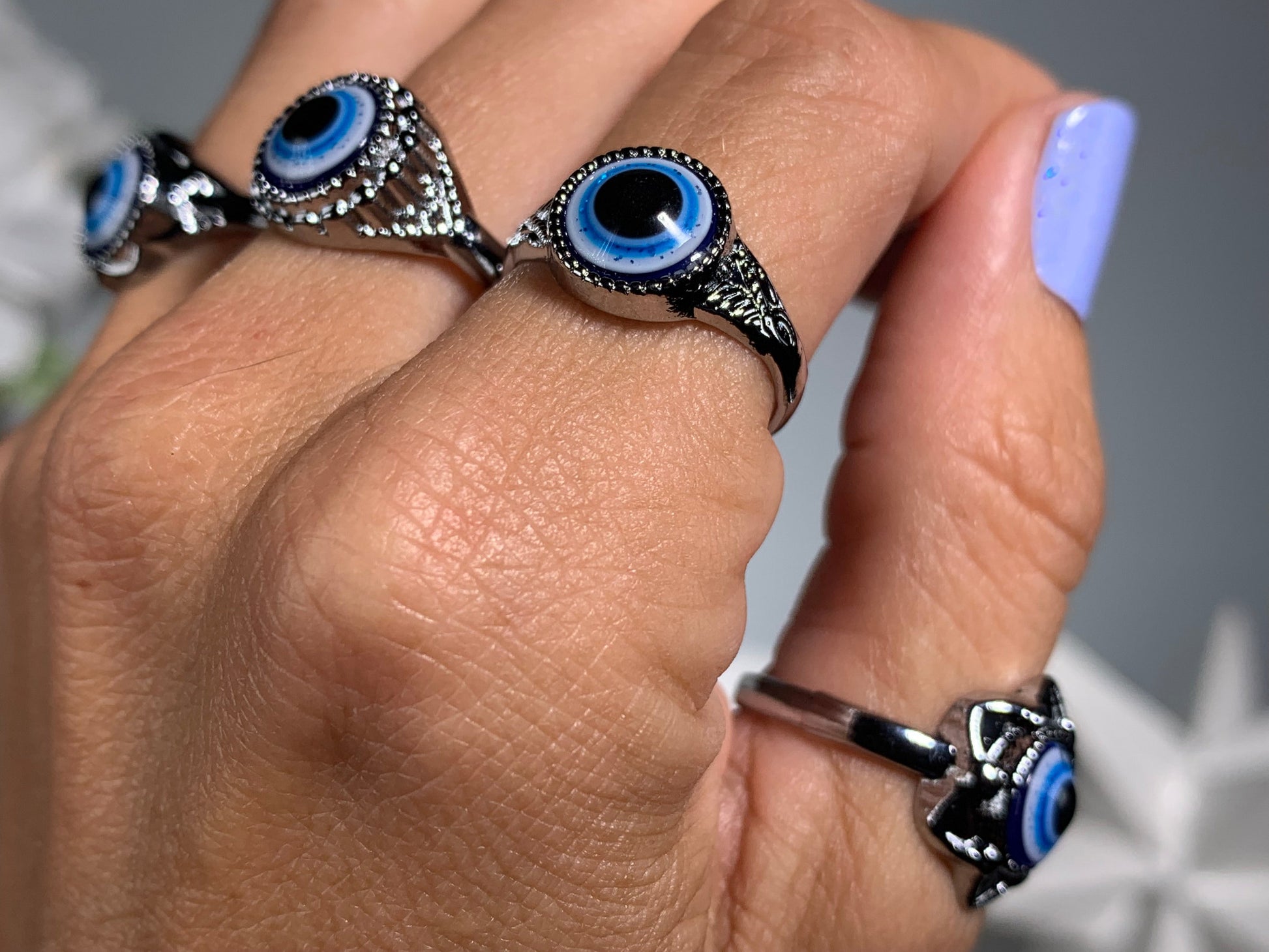 Close-up of hand with Protect Your Peace Silver Evil Eye Rings for energy and trust against a white gray floral background