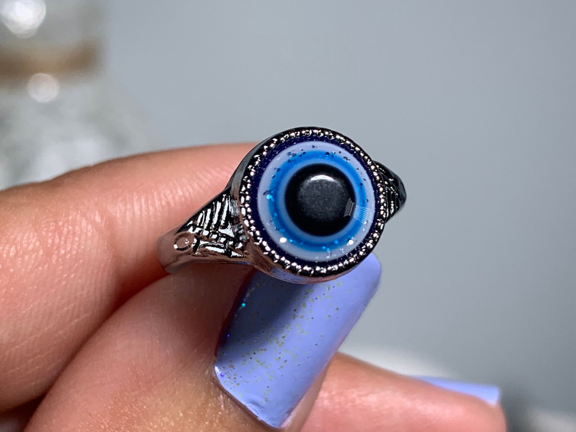 Close-up of hand with Protect Your Peace Silver Evil Eye Ring for energy and trust against a white gray floral background