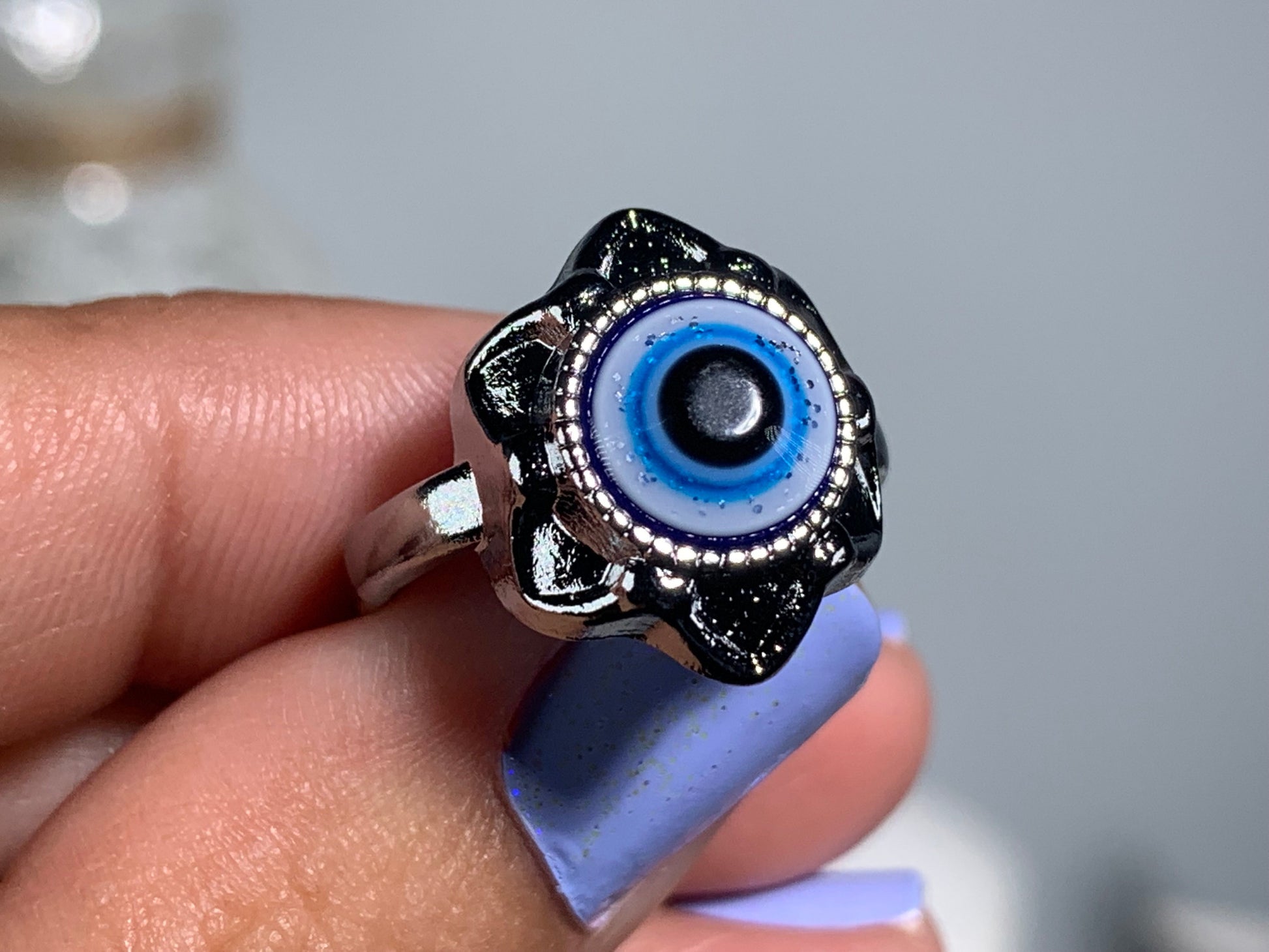 Close-up of hand with Protect Your Peace Silver Evil Eye Ring for energy and trust against a white gray floral background