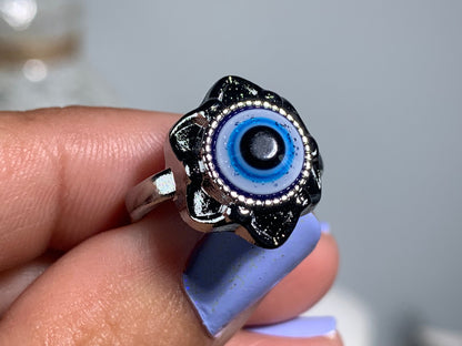 Close-up of hand with Protect Your Peace Silver Evil Eye Ring for energy and trust against a white gray floral background