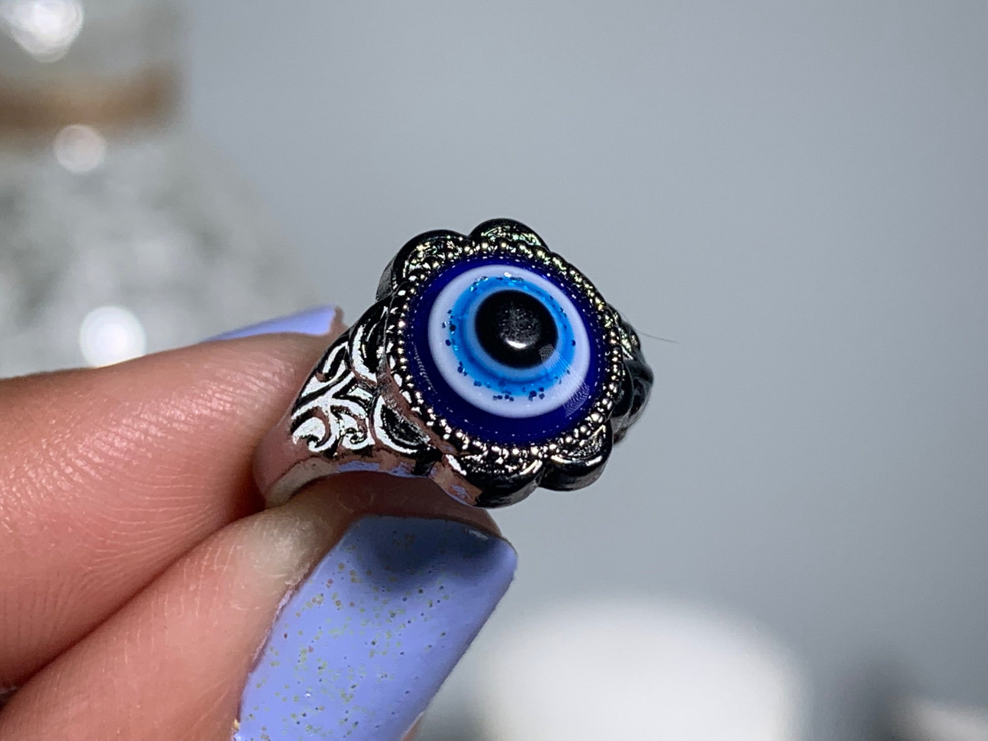 Close-up of hand with Protect Your Peace Silver Evil Eye Ring for energy and trust against a white gray floral background