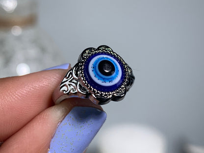 Close-up of hand with Protect Your Peace Silver Evil Eye Ring for energy and trust against a white gray floral background