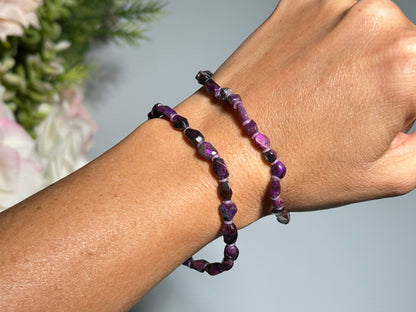 Wrist wearing a Purple Sugilite Bracelet for natural grounding crystal healing stone with floral background