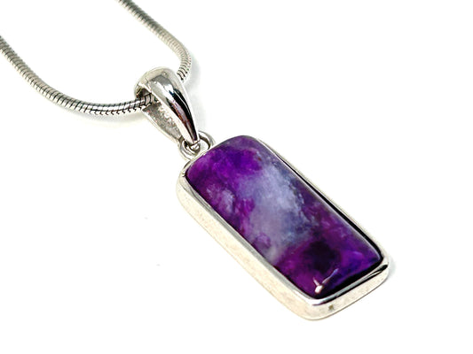 Purple Sugilite Crystal Pendant in Sterling Silver for meditation and energy work on table with white background