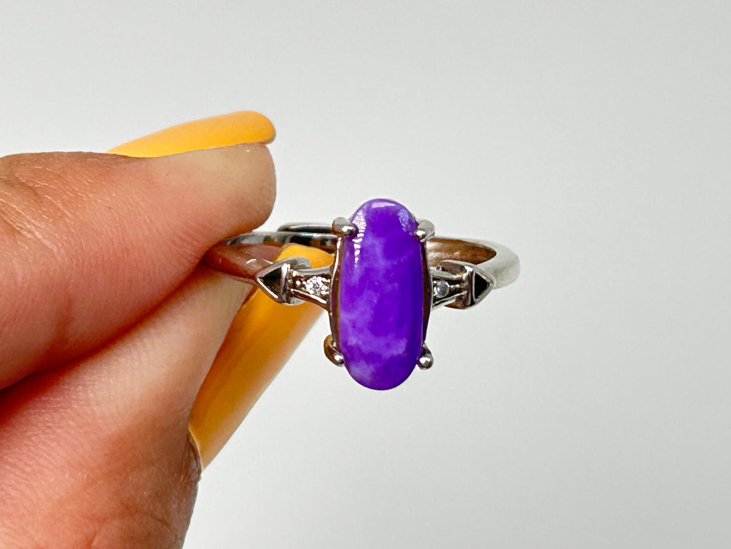 Fingers holding a Purple Sugilite Crystal in Sterling Silver Ring with Cubic Zirconia for natural grounding crystal healing stone with white background