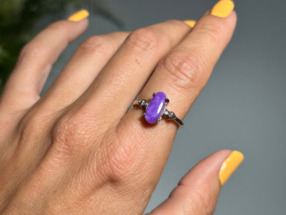 Close up of finger wearing a Purple Sugilite Crystal in Sterling Silver Ring with Cubic Zirconia for meditation and energy work with gray floral background
